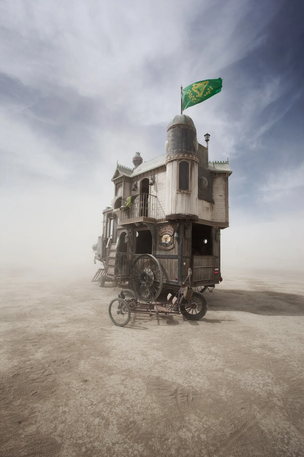 A Victorian house built as an art car, flying a green flag across the dusty playa