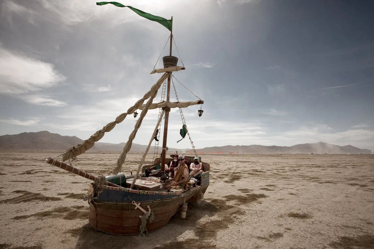 A pirate ship art car parked on the open playa, mountains behind