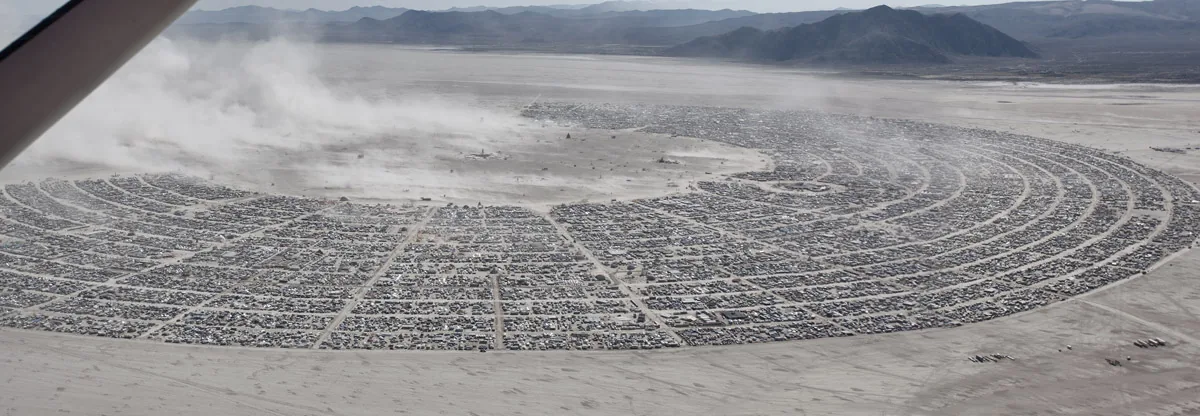 Aerial view of the arc of Black Rock City, with dust blowing across the desert