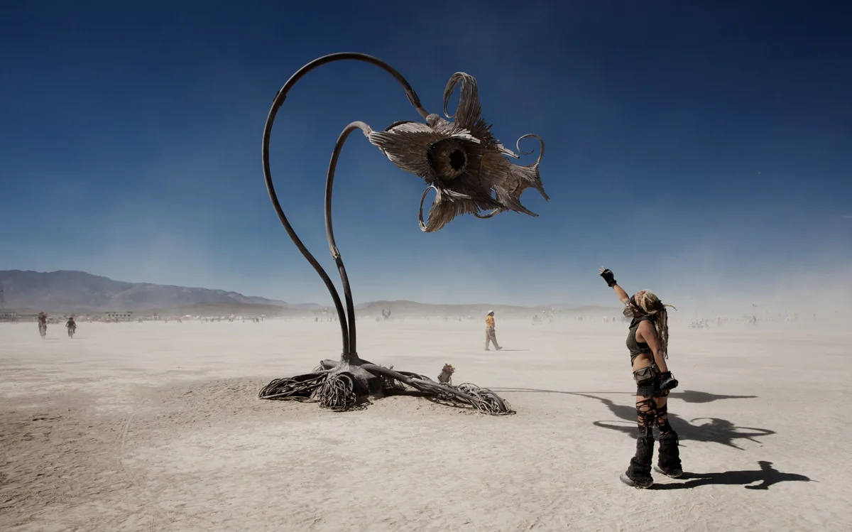 A giant metal flower sculpture, with a person reaching up toward it