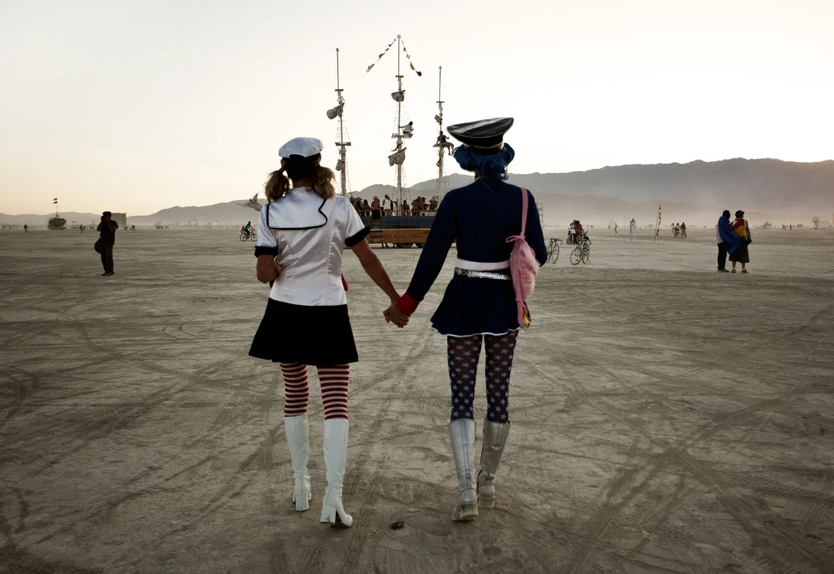 Two people in sailor costumes walking hand in hand toward a ship art car