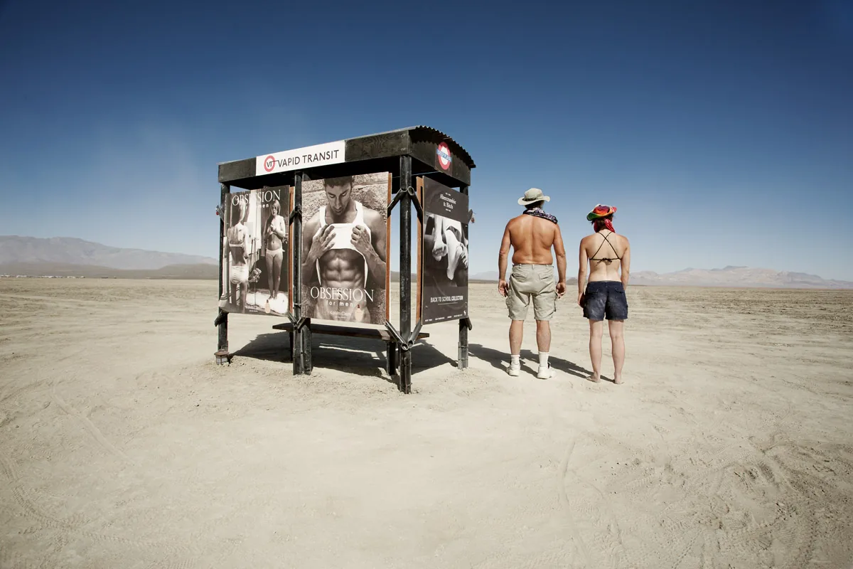 Two people looking at a bus stop installation in the open desert