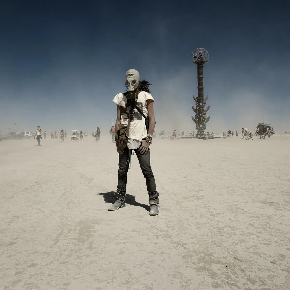A person in a gas mask standing in the dust, a tower sculpture behind
