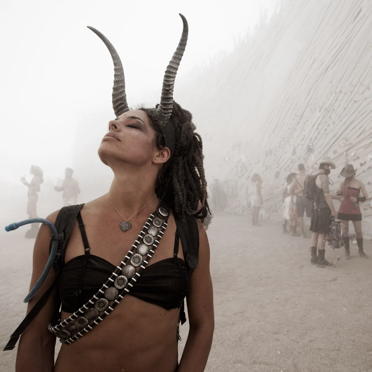 A woman with horns and a bandolier, eyes closed, in a dust storm