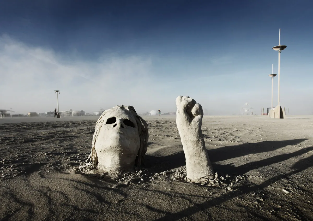 A sculpted face and fist rising out of the playa
